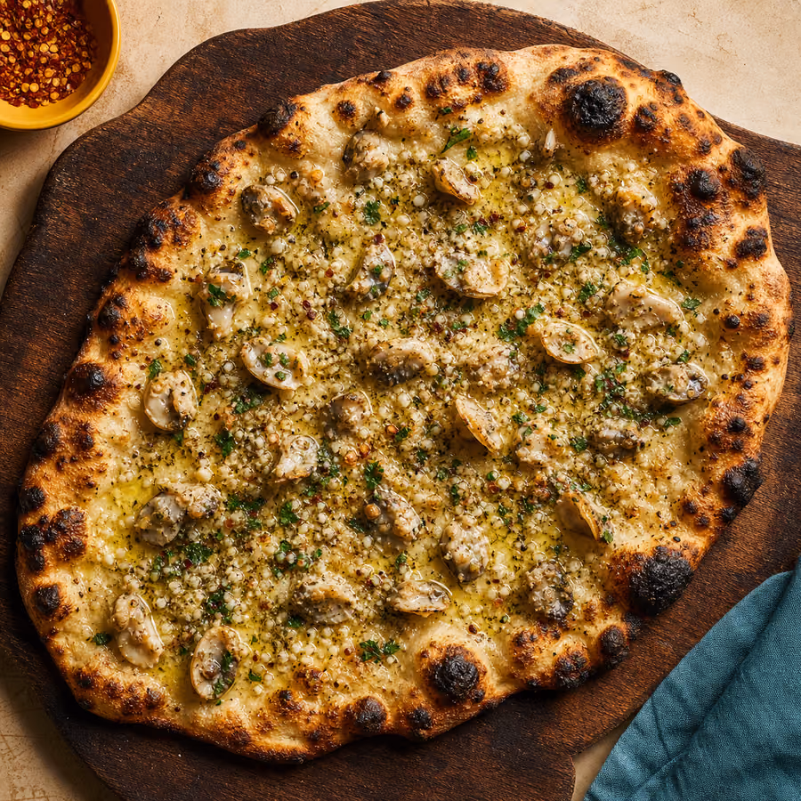New Haven White Clam Pizza – dünne, stark gecharrte ovale apizza mit Venusmuscheln, Knoblauch, Olivenöl und geriebenem Pecorino auf einem Holzbrett